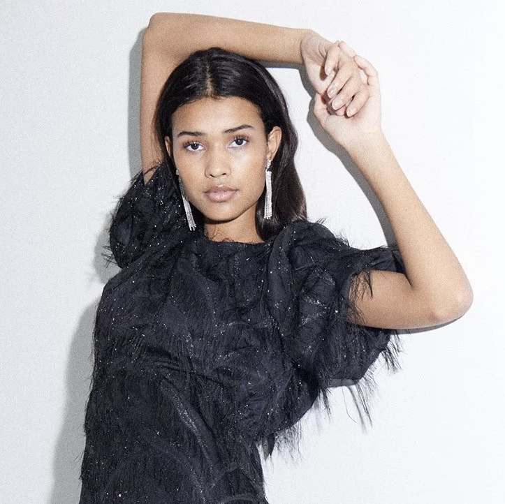 A woman in a black party dress and sparkly earrings poses for the camera.